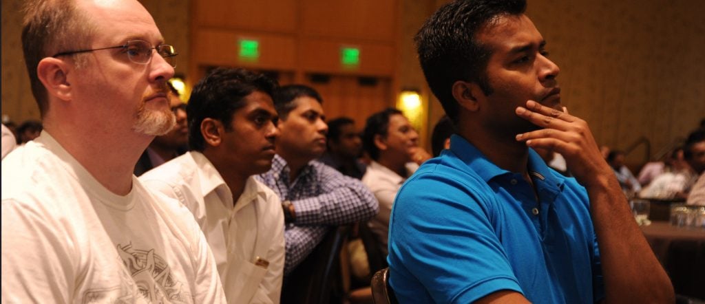 Large group listens attentively to a presentation in a large room. Photo by Wonderlane via Unsplash