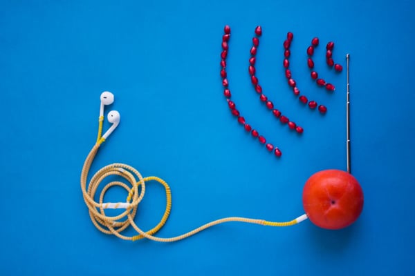 Image of a tomato with earbuds plugged into the tomato on the left side and an antenna sticking up from the top of the tomato with a signal emitting from the antenna made from pomegranate seeds.