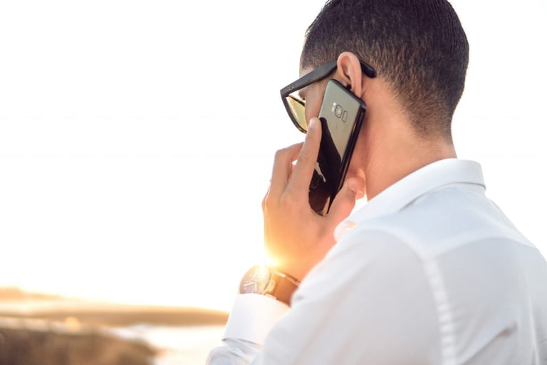 Photo of man talking on a mobile phone while overlooking a nature scene. Image source: Hassan Ouajbir via Unsplash.