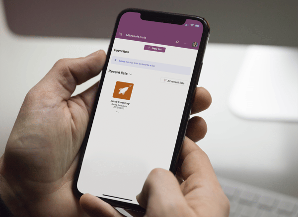 A person holding a phone with the Microsoft Lists application displayed